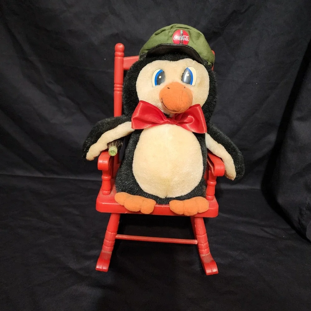1997 vintage Coca-Cola penguin plush toy sitting in a‎ red rocking chair.
